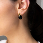 A close-up of a model's ear wearing a minimalist black and gold drop earring.