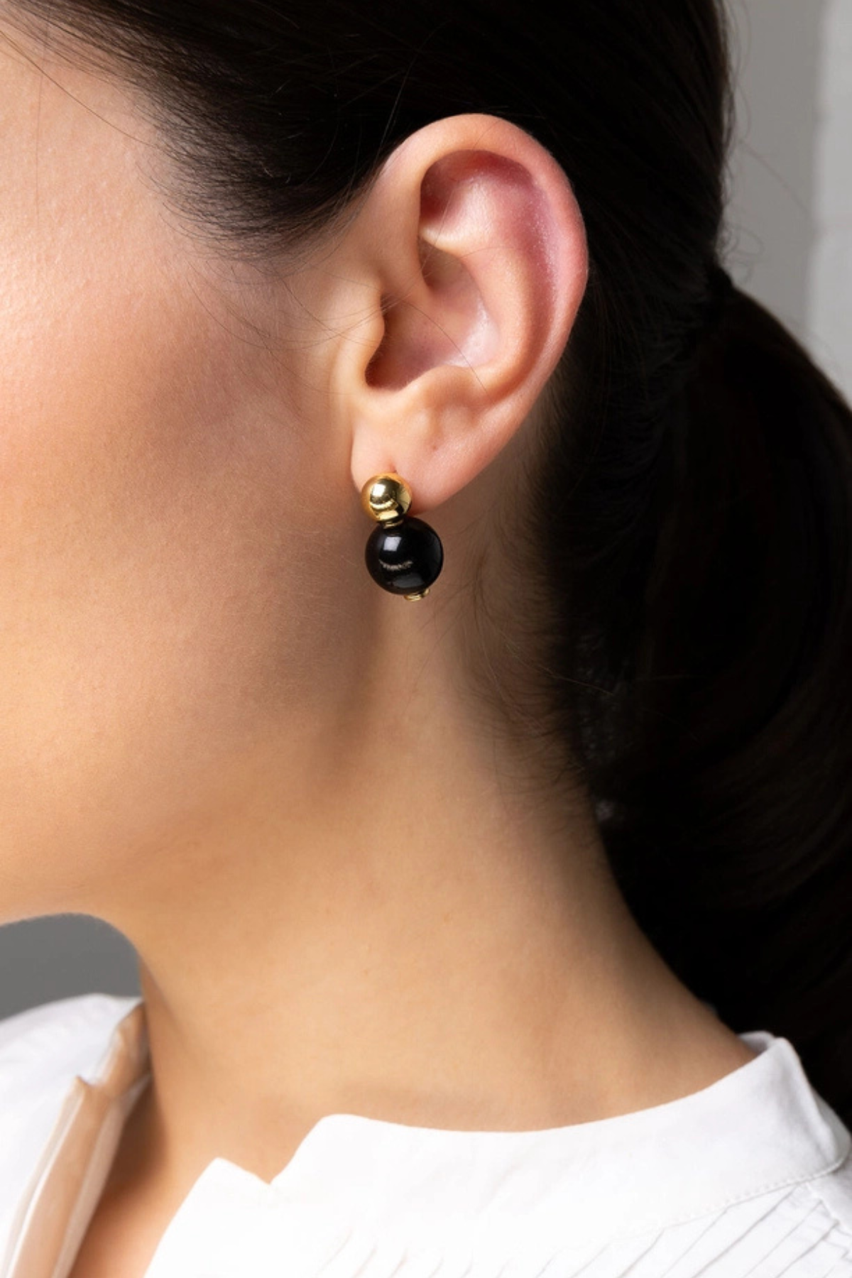 A close-up of a model's ear wearing a minimalist black and gold drop earring.
