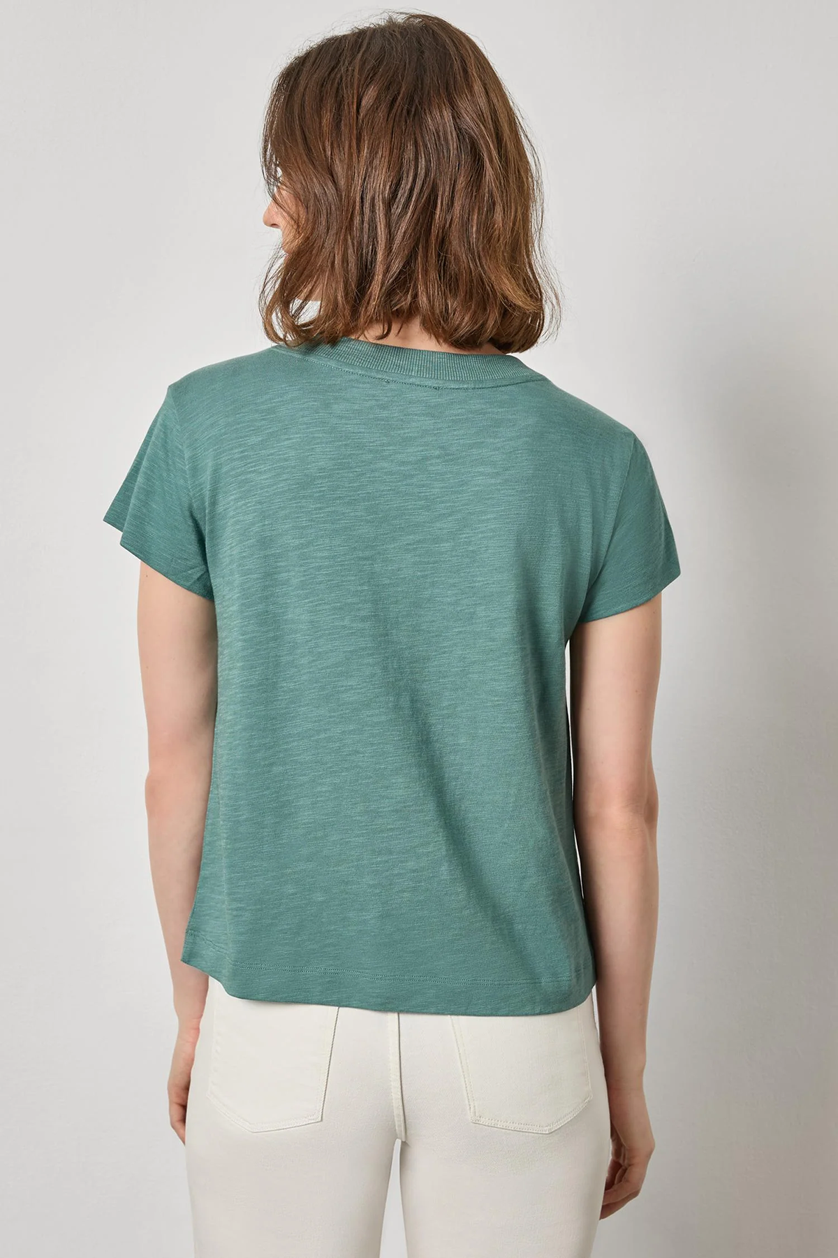 Person wearing a teal t-shirt and white pants against a plain background