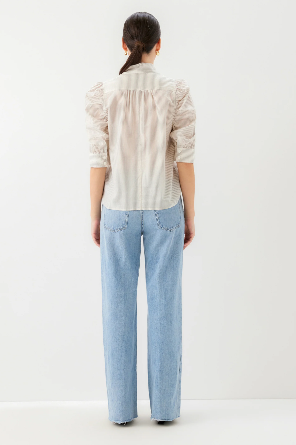 Person wearing a light-colored shirt and blue jeans on a white background
