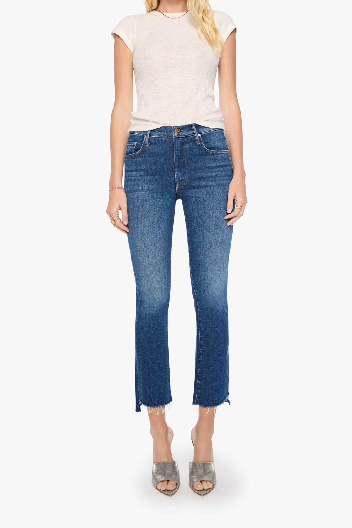 A model wearing a cream-colored short-sleeve top and blue cropped flare jeans with side slits, paired with silver heeled sandals, against a plain white background.