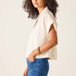 Woman wearing a beige sleeveless top and blue jeans against a plain background