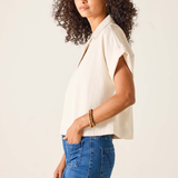 Woman wearing a beige sleeveless top and blue jeans against a plain background