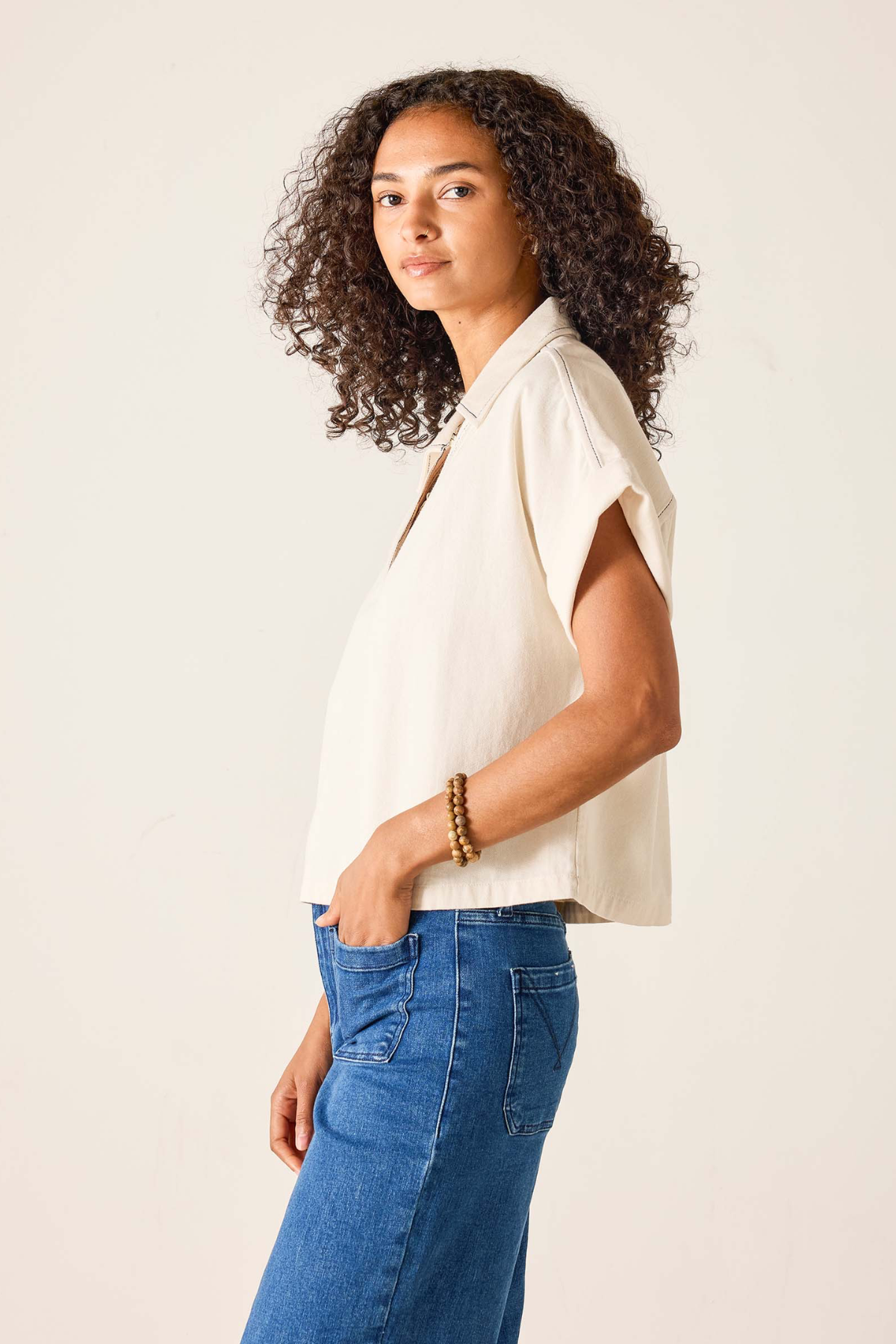 Woman wearing a beige sleeveless top and blue jeans against a plain background