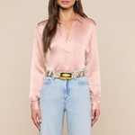 Woman wearing a pink satin shirt and light blue jeans with a beige background