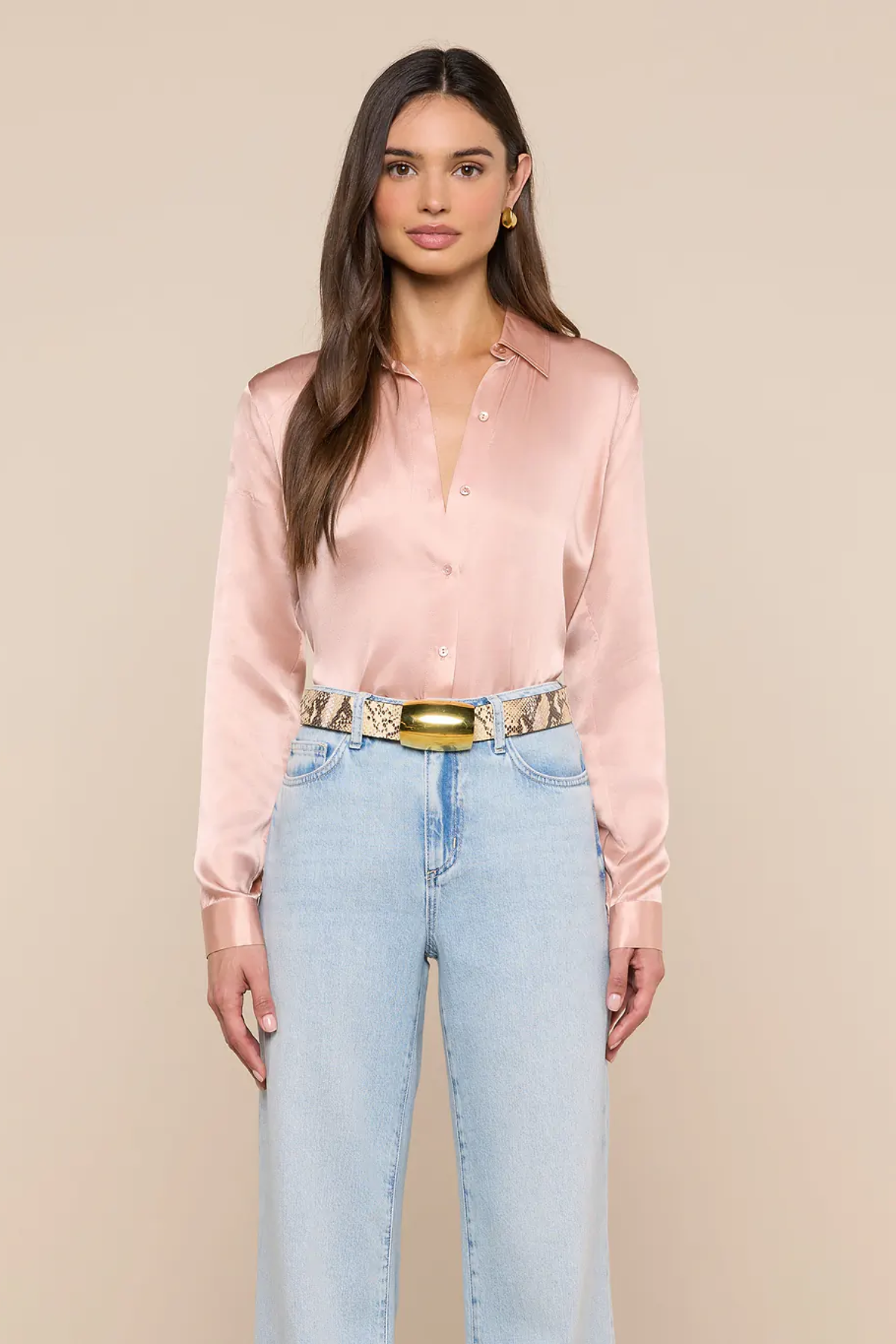 Woman wearing a pink satin shirt and light blue jeans with a beige background