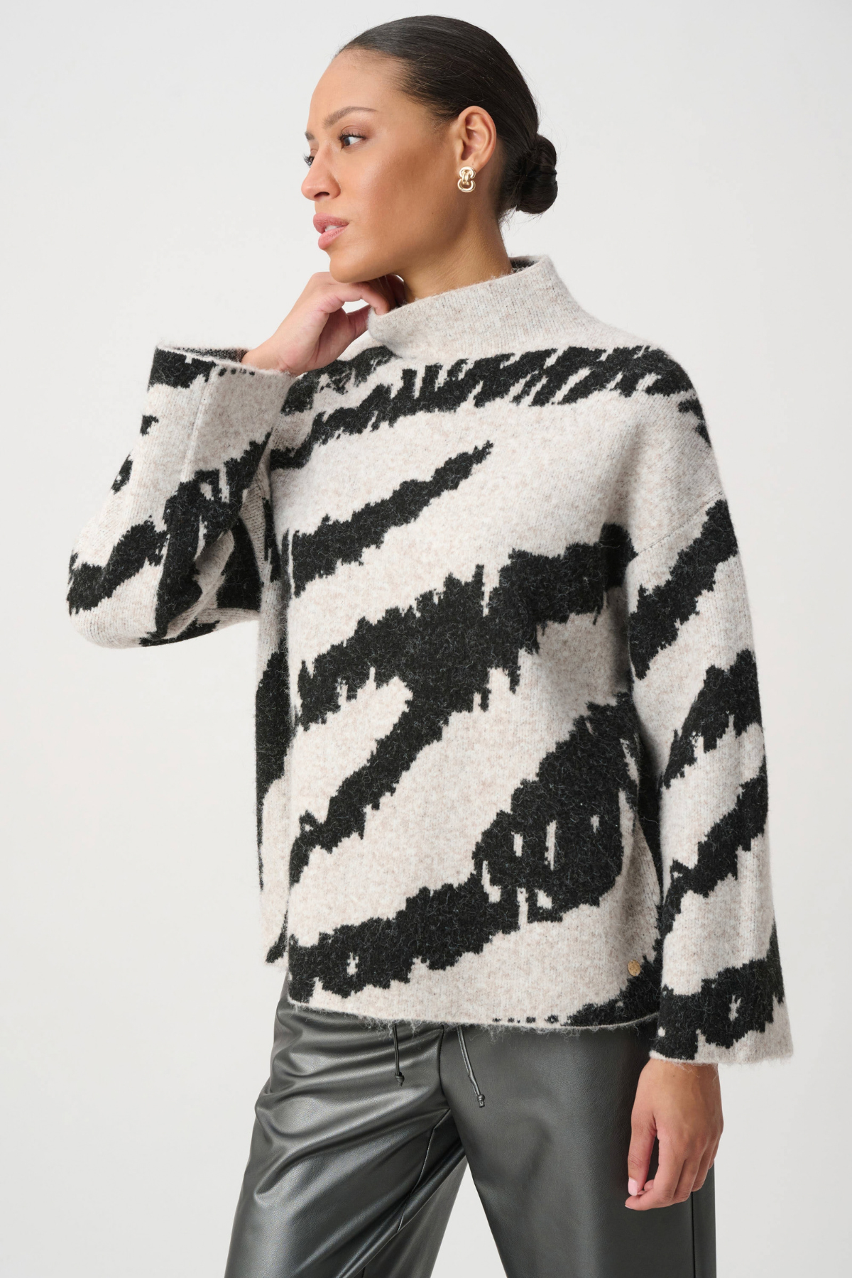 A woman wearing a fuzzy knit sweater with a black and off-white zebra-like pattern, paired with dark metallic pants, against a plain light gray studio background.