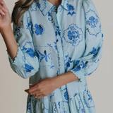 Woman wearing a light blue dress with blue floral patterns against a neutral background