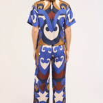 A woman viewed from the back wearing a matching short-sleeve top and wide-leg pants set with a bold abstract pattern in blue, brown, cream, and white on a light studio background.
