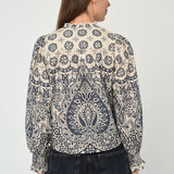 Woman wearing a patterned long sleeve blouse with a gathered neckline in neutral tones