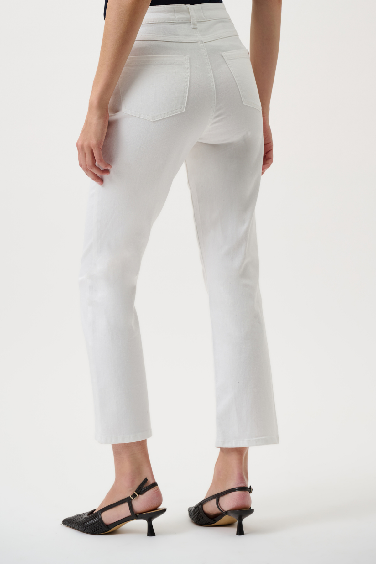 White cropped jeans shown from the back on a model, paired with black kitten-heel sandals against a clean white studio background.