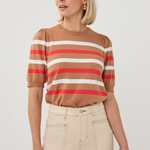 Woman wearing a brown, red, and white striped shirt with beige pants on a light gray background
