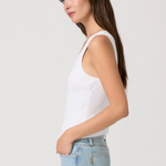 Woman wearing a white tank top and light blue jeans against a plain background