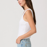 Woman wearing a white tank top and light blue jeans against a plain background