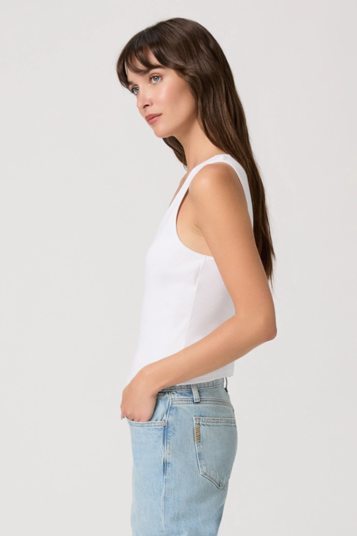 Woman wearing a white tank top and light blue jeans against a plain background