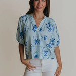 Woman wearing a light blue blouse with floral patterns on a plain background