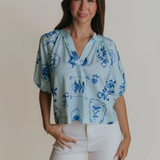 Woman wearing a light blue blouse with floral patterns on a plain background