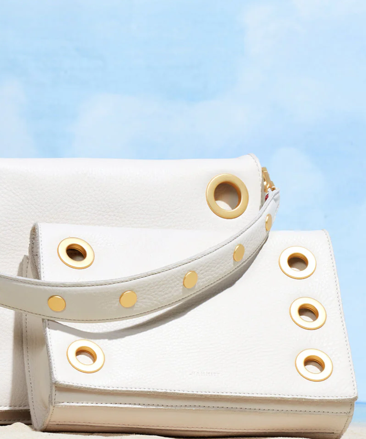 White handbag with gold accents on a sandy surface with a blue sky background