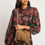 Woman wearing a floral dress holding a brown fringed bag against a white background