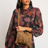 Woman wearing a floral dress holding a brown fringed bag against a white background