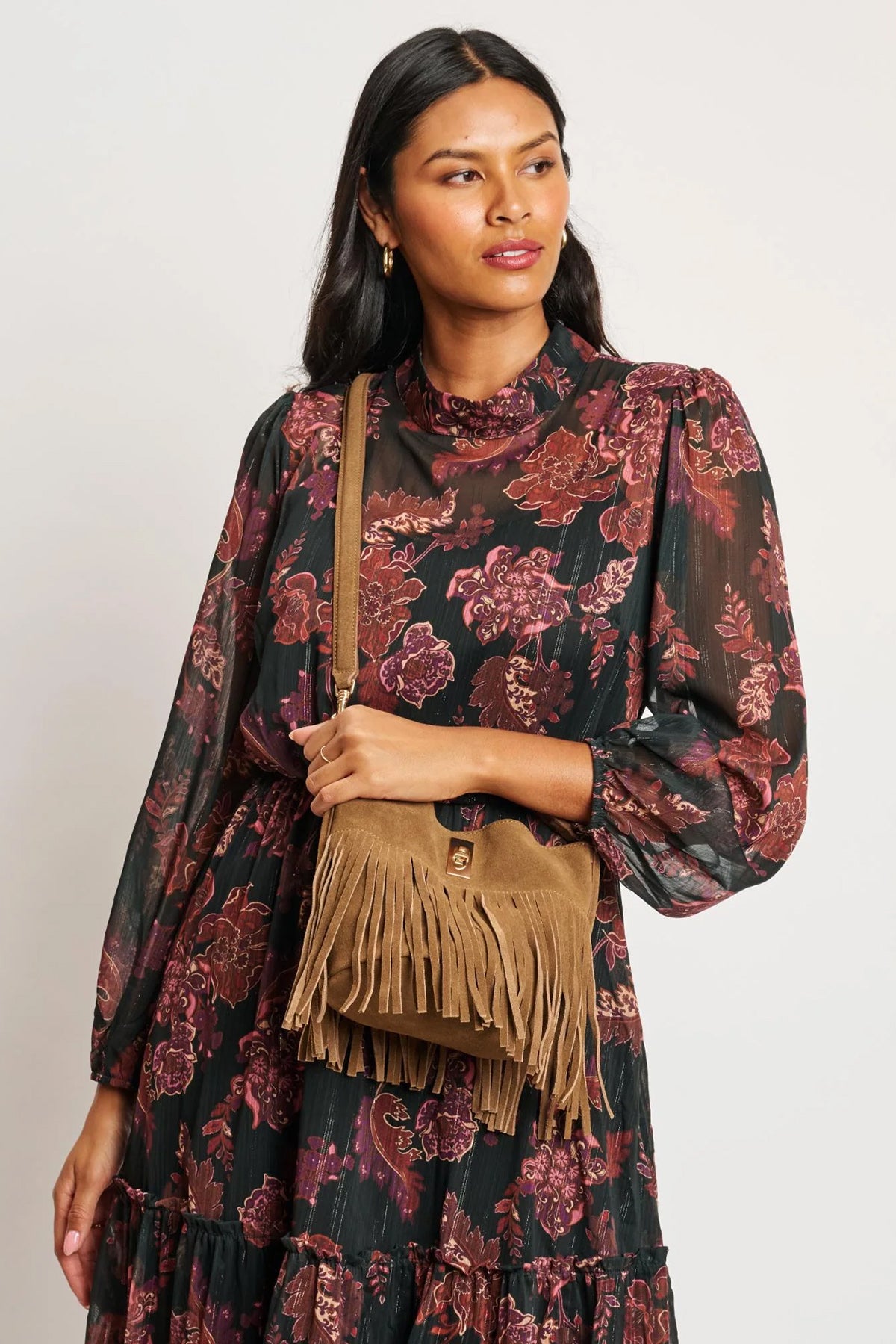 Woman wearing a floral dress holding a brown fringed bag against a white background