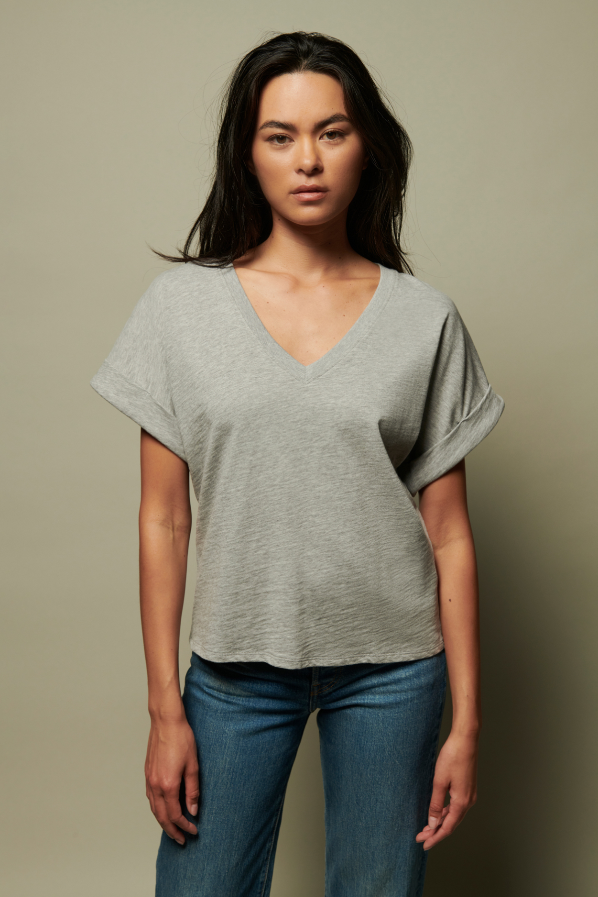 Woman wearing a gray oversized t-shirt and blue jeans against a beige background
