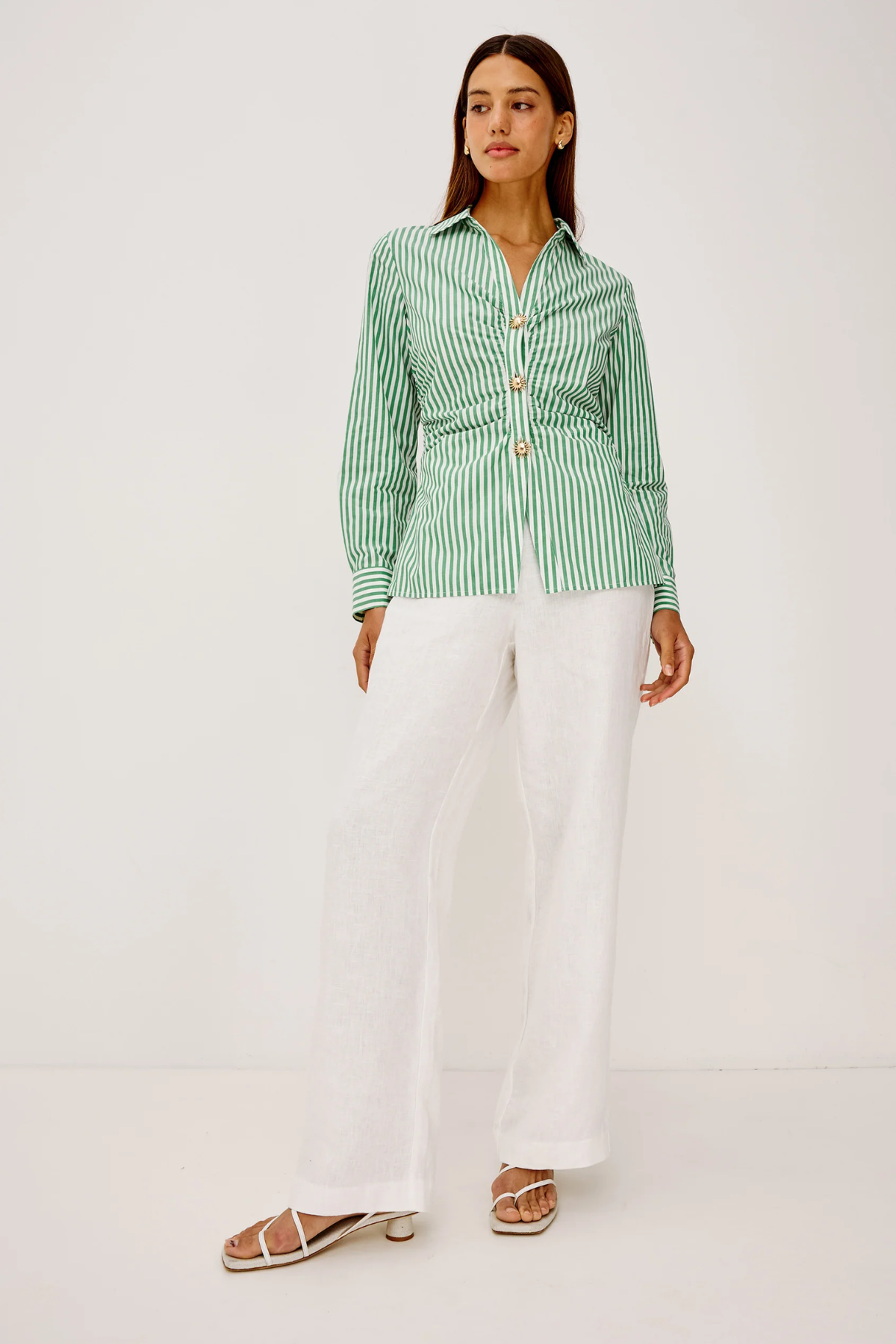 Woman wearing a green and white striped shirt with white pants on a white background