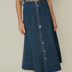 Person wearing a blue denim skirt with a patterned top on a neutral background