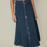 Person wearing a blue denim skirt with a patterned top on a neutral background