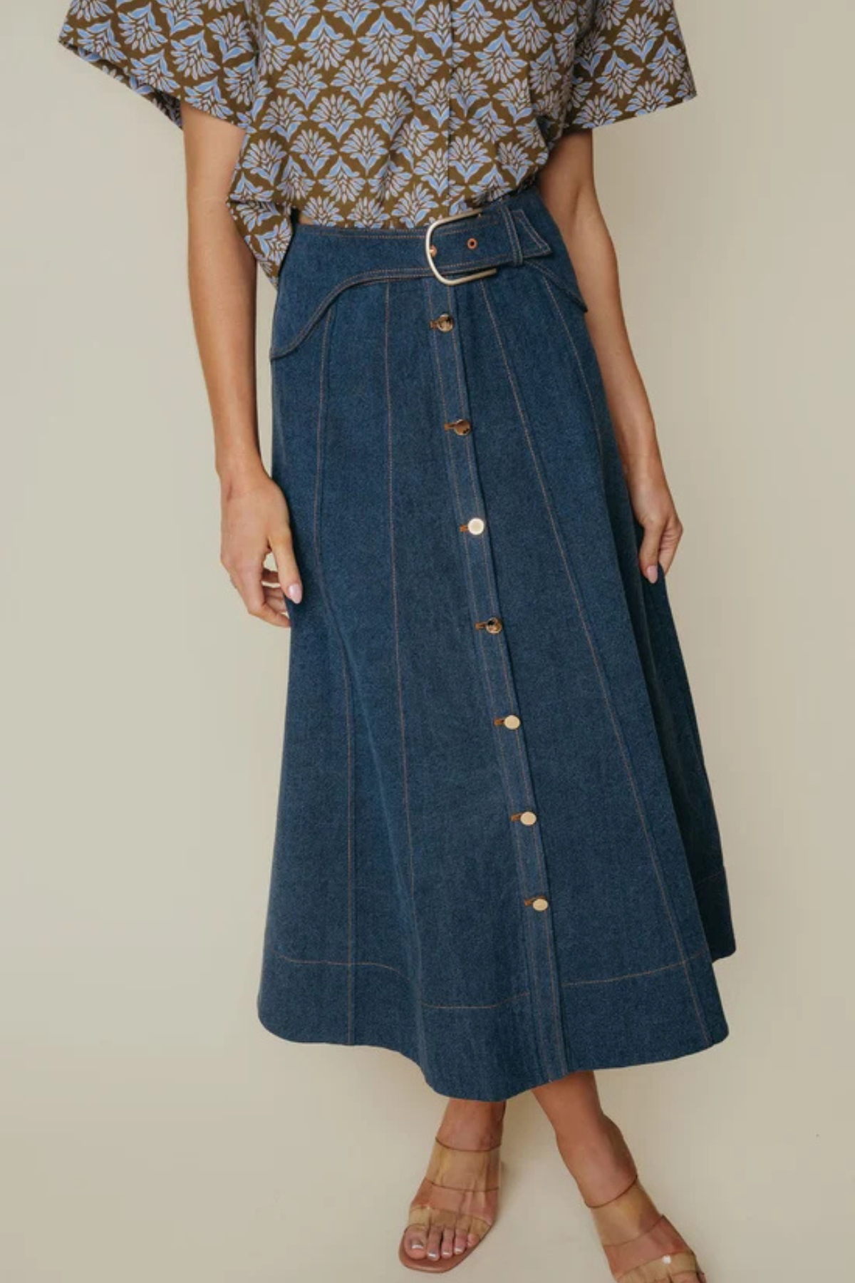 Person wearing a blue denim skirt with a patterned top on a neutral background