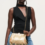 Woman holding a gold fringe handbag against a plain background
