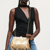 Woman holding a gold fringe handbag against a plain background