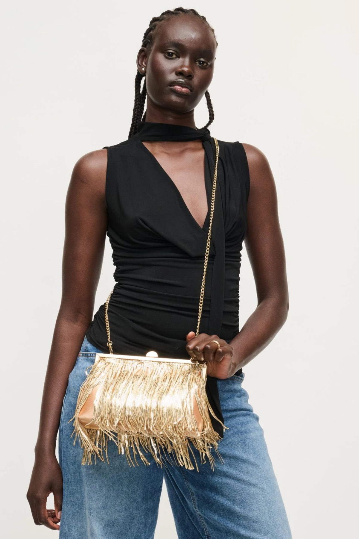 Woman holding a gold fringe handbag against a plain background