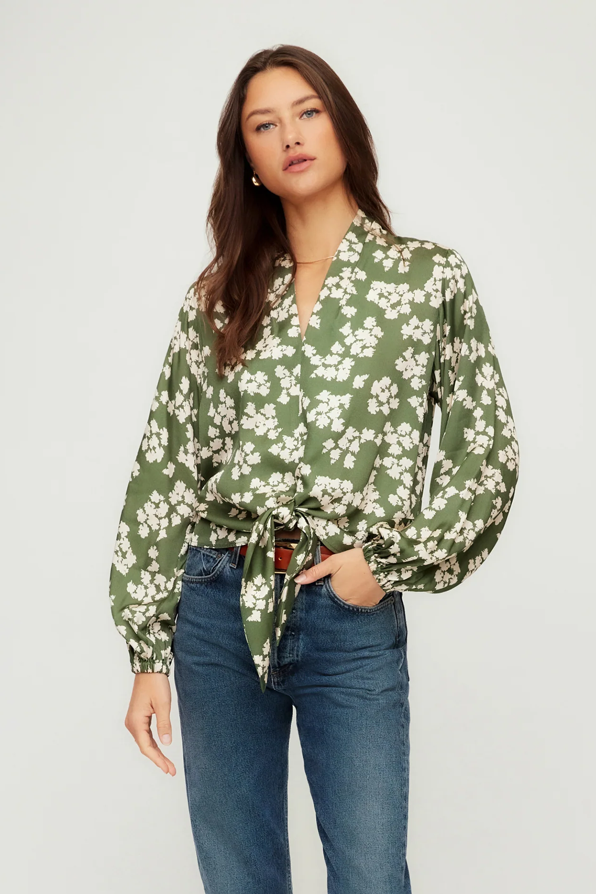 Woman wearing a green floral blouse and blue jeans on a white background