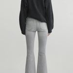 A model shown from the back wearing a dark charcoal gray knit sweater, light gray flared jeans, and black pointed-toe heels against a light gray studio background.