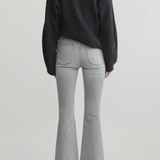 A model shown from the back wearing a dark charcoal gray knit sweater, light gray flared jeans, and black pointed-toe heels against a light gray studio background.