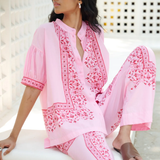 Woman wearing a pink embroidered outfit sitting on a white surface.