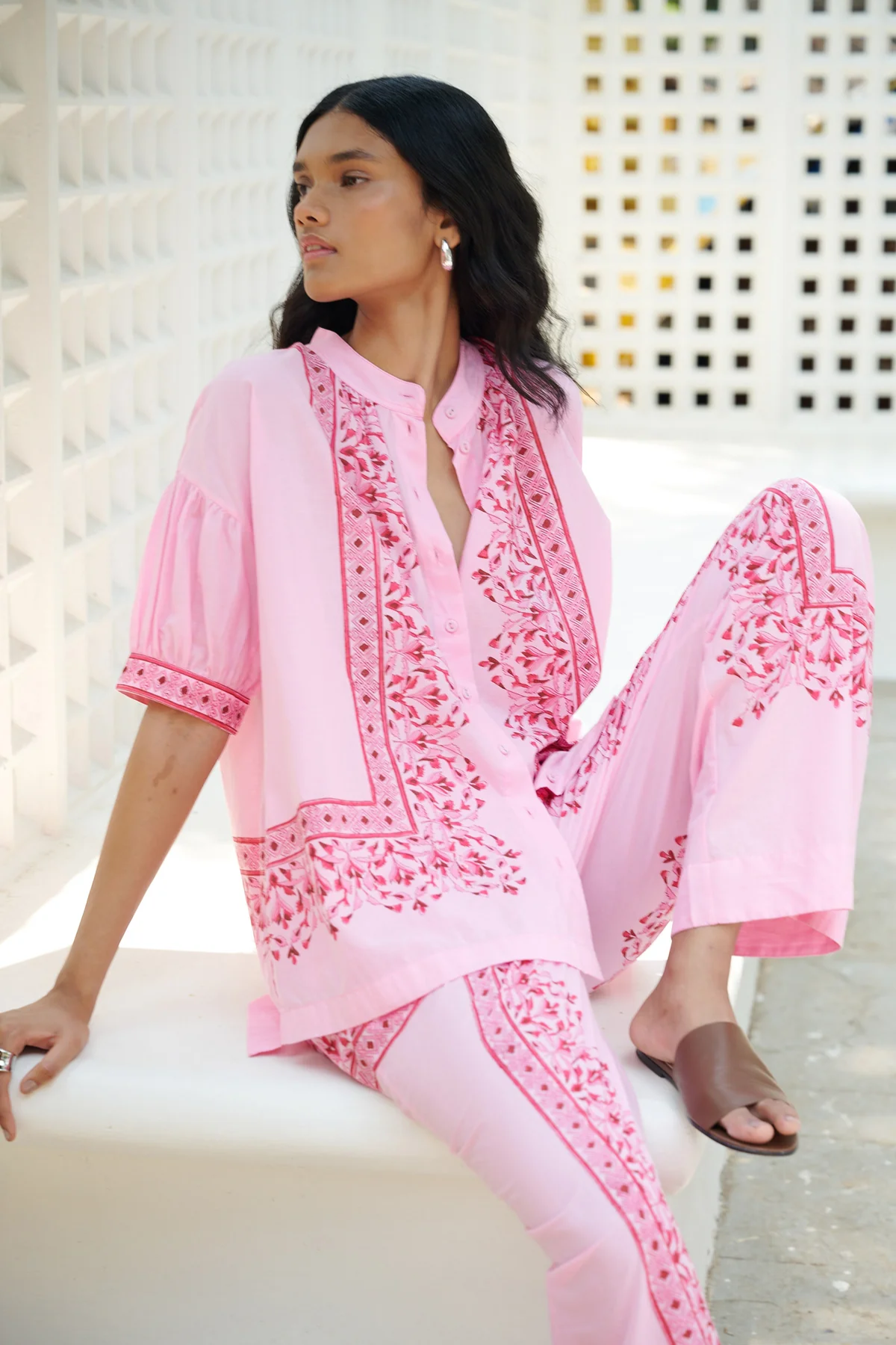 Woman wearing a pink embroidered outfit sitting on a white surface.