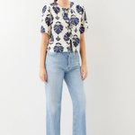 Woman wearing a patterned blouse and light blue jeans on a white background