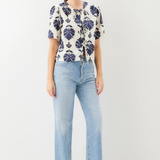 Woman wearing a patterned blouse and light blue jeans on a white background