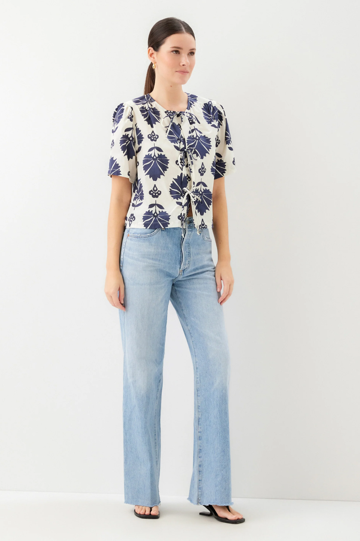 Woman wearing a patterned blouse and light blue jeans on a white background