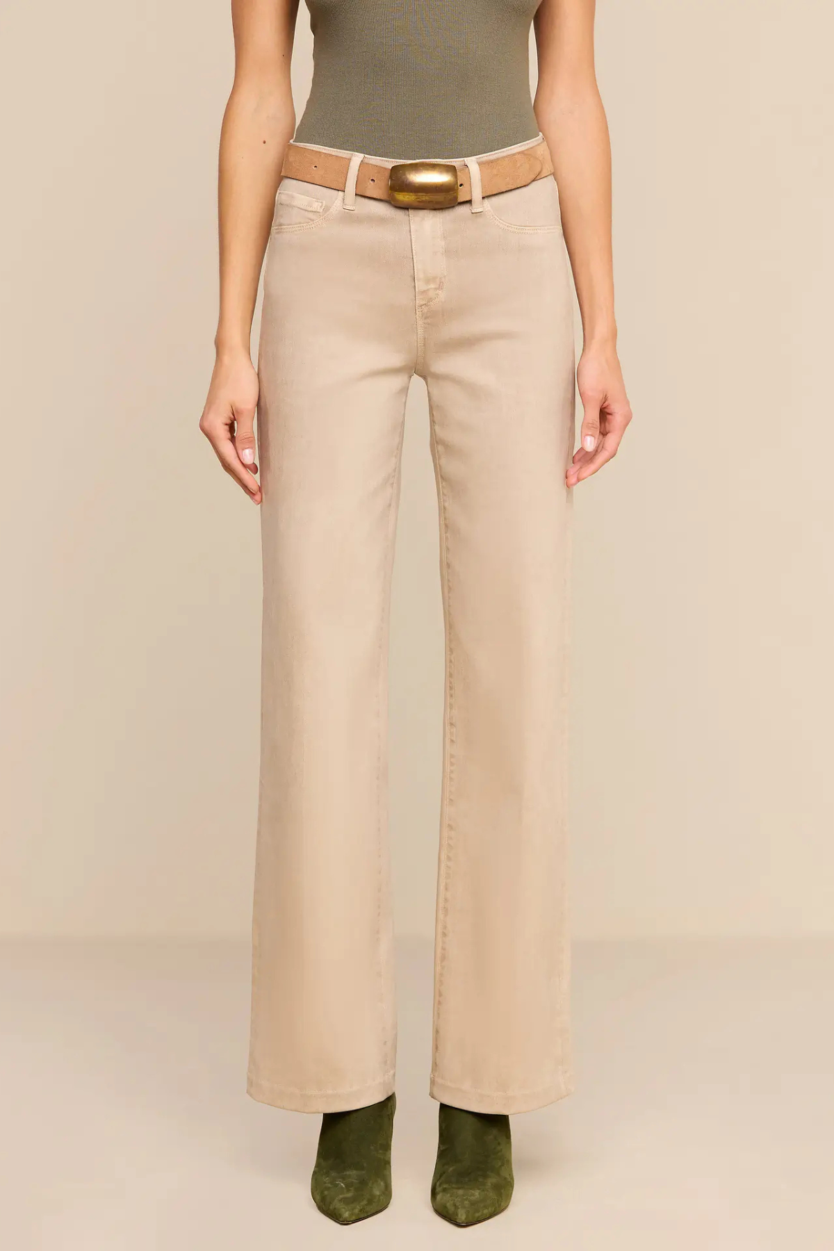 A model wearing beige wide-leg cropped pants with a tan belt and a gold buckle, paired with an olive green top and green suede boots, against a solid beige background.