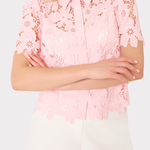 Person wearing a pink lace blouse with white shorts on a light gray background