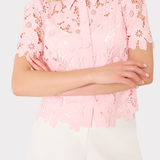 Person wearing a pink lace blouse with white shorts on a light gray background
