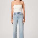 Woman wearing a white strapless top and light blue jeans on a plain background