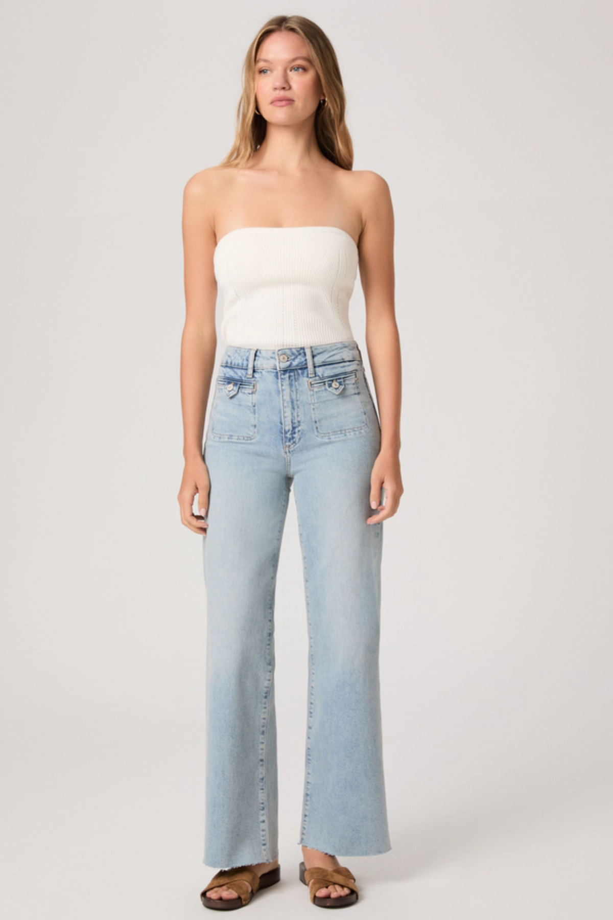 Woman wearing a white strapless top and light blue jeans on a plain background