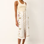 Woman wearing a cream tank top and white floral skirt on a white background