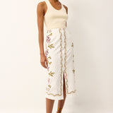 Woman wearing a cream tank top and white floral skirt on a white background