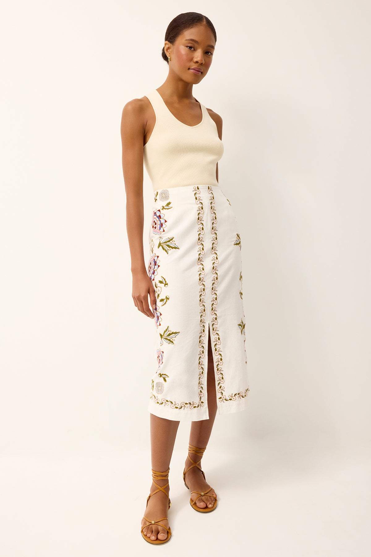 Woman wearing a cream tank top and white floral skirt on a white background