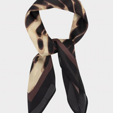 A lightweight silk scarf with an abstract organic pattern in black, dark brown, and beige, styled in a loop on a light gray background.